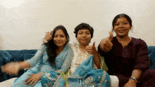 three women are sitting on a couch giving thumbs up