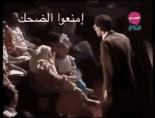a group of people are sitting in a dark room with arabic writing on the bottom