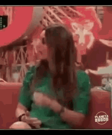 a woman in a green shirt is sitting on a red couch and holding her breast .