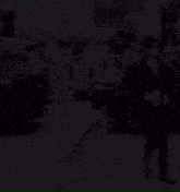 a man in a black jacket is walking down a street with a cup of coffee in his hand .