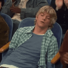 a man in a plaid shirt is sleeping in a theatre seat