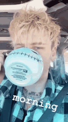 a man wearing a plaid shirt is drinking from a blue cup with stitches on it
