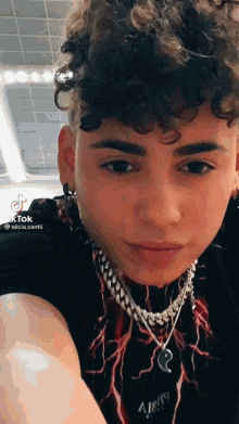 a young man with curly hair wearing a necklace and earrings