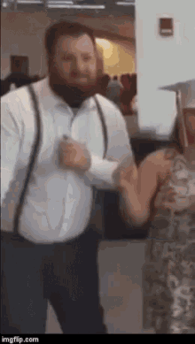 a man with a beard wearing suspenders is dancing with a woman .