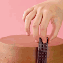 a person 's hand is holding a chocolate bar on top of a cake