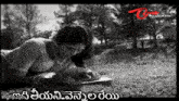 a black and white photo of a woman laying on the grass writing on a piece of paper .