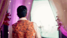 a man in a vest is standing in front of a mirror in a room with purple lights .