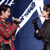 a man in a plaid shirt is holding a microphone and talking to another person