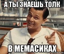 a man is sitting in a chair and pointing at the camera with a meme in russian .