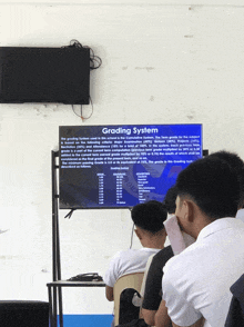 a group of students are sitting in front of a tv screen that says grading system