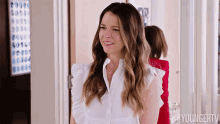 a woman in a white shirt is standing in a hallway smiling .