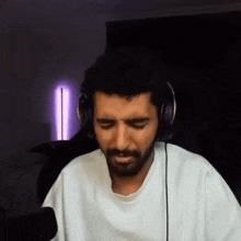 a man with a beard wearing headphones and a white shirt is sitting in front of a microphone .