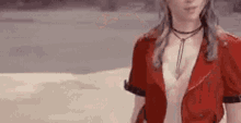 a woman wearing a red jacket and a choker is standing on a sandy beach .