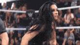 a woman stands in a wrestling ring with a w logo on the wall behind her