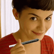 a woman in a red shirt is smiling while holding a cigarette in her hand .