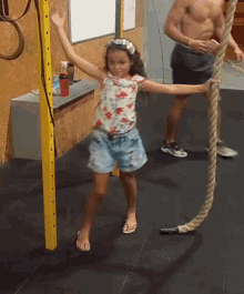 a little girl is holding a rope in a gym while a man watches