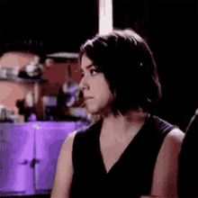 a woman in a black dress is sitting in a dark room looking at something .