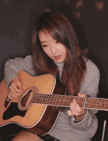 a young woman is playing an acoustic guitar in a dark room