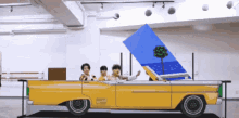 a group of people are riding in a yellow convertible car
