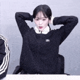 a woman wearing a black adidas jacket is sitting at a table