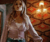 a woman in a purple top and jeans is standing in front of a wall with a patterned wallpaper .