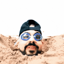a man with a beard wearing a hat and goggles is buried in the sand