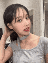 a woman wearing a grey top with a choker around her neck is looking at the camera