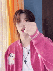 a young man in a pink jacket is making a heart shape with his finger .