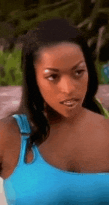 a woman in a blue tank top is looking at the camera and making a funny face .