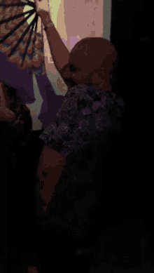 a bald man in a floral shirt is holding up a fan
