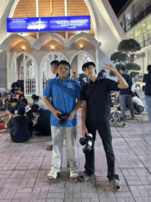 two men standing in front of a building with a blue sign that says ' a ' on it