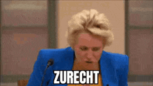 a woman in a blue jacket is giving a speech in front of a microphone and saying zurecht .