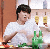 a young man is sitting at a table with a bottle of corona beer