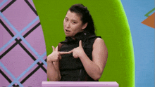 a woman in a black vest is pointing at herself