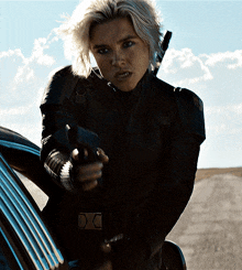 a woman in a black jacket is pointing a gun at someone