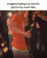 a man in an orange shirt is hugging another man in a crowd of people .
