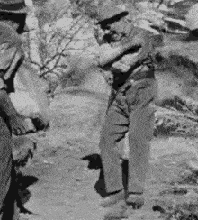 a man in a hat is standing in the dirt with his arms crossed .