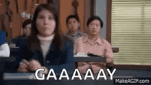 a group of people are sitting in a classroom with the words gaaaay on the screen .