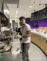 a man in a white shirt stands in a kitchen with a taco bell logo in the background