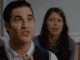 a man and a woman are sitting in a room and the man is wearing a vest