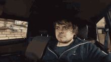 a man in a blue adidas jacket sits in a car seat