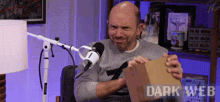 a man is holding a cardboard box in front of a microphone with the words dark web on the bottom right