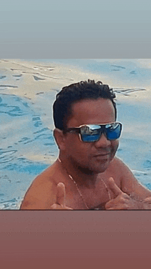 a shirtless man wearing sunglasses is giving a thumbs up in a pool .