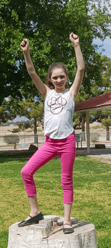 a girl in a minnie mouse shirt is standing on a tree stump