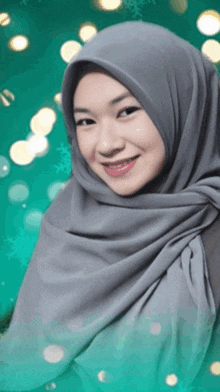 a woman wearing a gray hijab is smiling for the camera