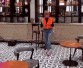 a woman in an orange vest is walking in a room with tables and chairs