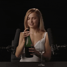 a woman in a white tank top holds a bottle of wine and a glass of wine