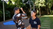 a woman wearing a girl power shirt is standing next to a man in a camouflage shirt