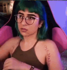 a girl with green hair and glasses is sitting in a pink chair .