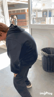 a man in a black hoodie is bending over next to a black trash can